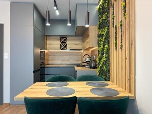 A modern kitchen with a wooden countertop, green chairs, and pendant lighting. - Six StarS|Executive Business Suite|6 min to Centre (Пловдив)