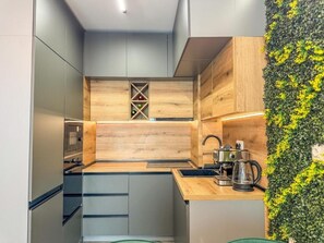 A compact kitchen with a wooden accent wall, a built-in wine rack, and a coffee maker on the counter. - Six StarS|Executive Business Suite|6 min to Centre (Пловдив)