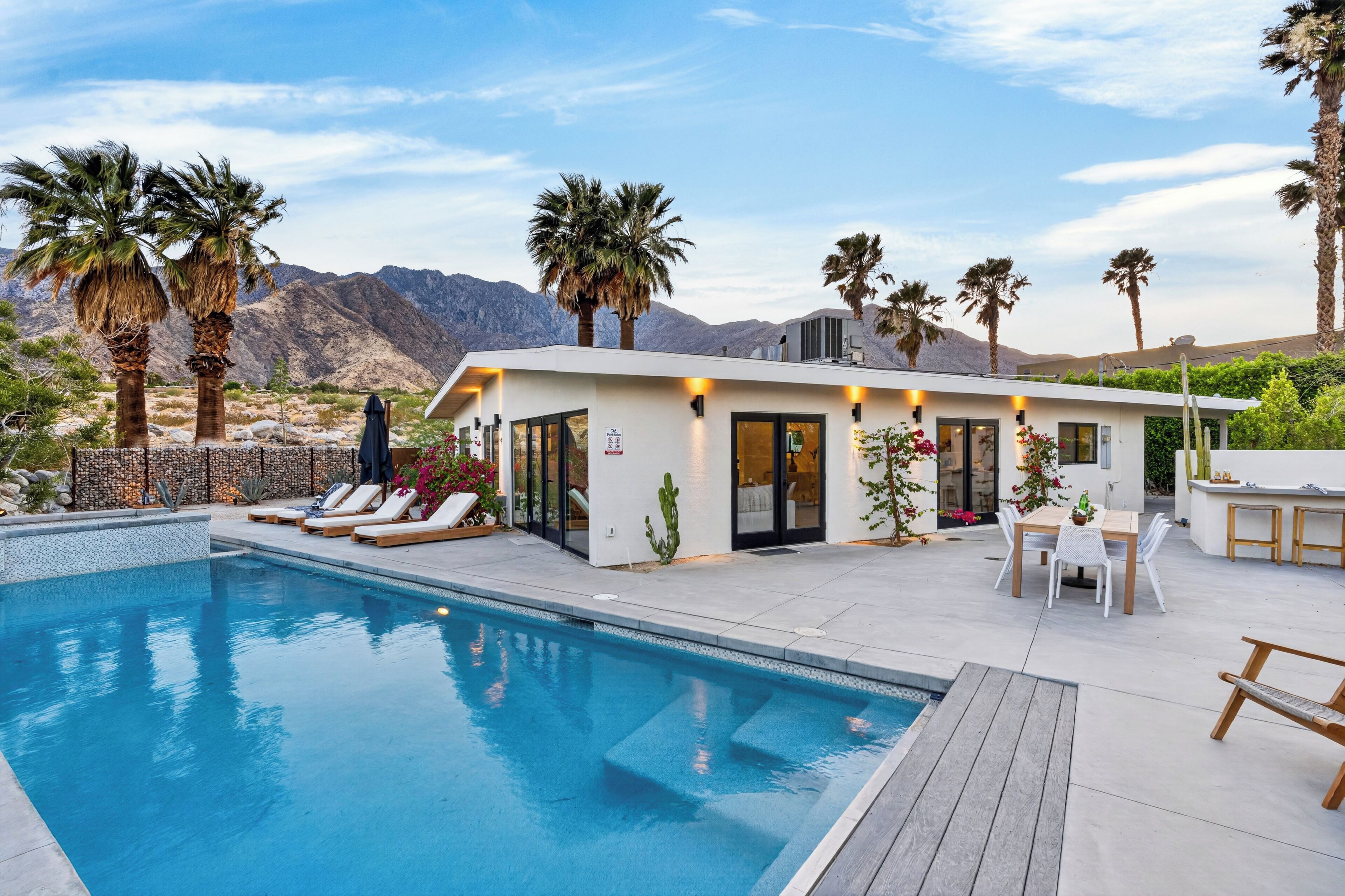 Un espace moderne aménagé au bord de la piscine, comprenant une piscine, des chaises longues et un bâtiment doté de portes vitrées.