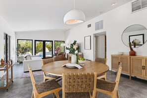 Een moderne eetruimte met een ronde houten tafel, geweven stoelen en een hanglamp.