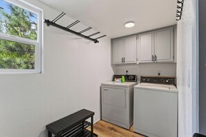 A laundry room with two washing machines, a dryer, and a small table. - Hot Tub + Game Room + Firepit • Near Bear Mountain + Lake | Balboa Big Bear (Big Bear Lake)