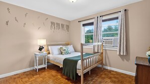 Un dormitorio con una cama litera, una mesita de noche con lámpara, una ventana con cortinas y una pared decorada con motivos de hojas.