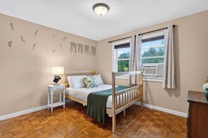 A bedroom with a bunk bed, a bedside table with a lamp, a window with curtains, and a wall with leaf decals. - Firepit + Grill + Chef Kitchen | Creek + Waterfalls | Ohana Nature Escape (Catskill)