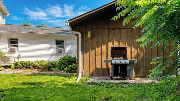 Un patio trasero con una parrilla de madera, una casa con revestimiento blanco y un césped.