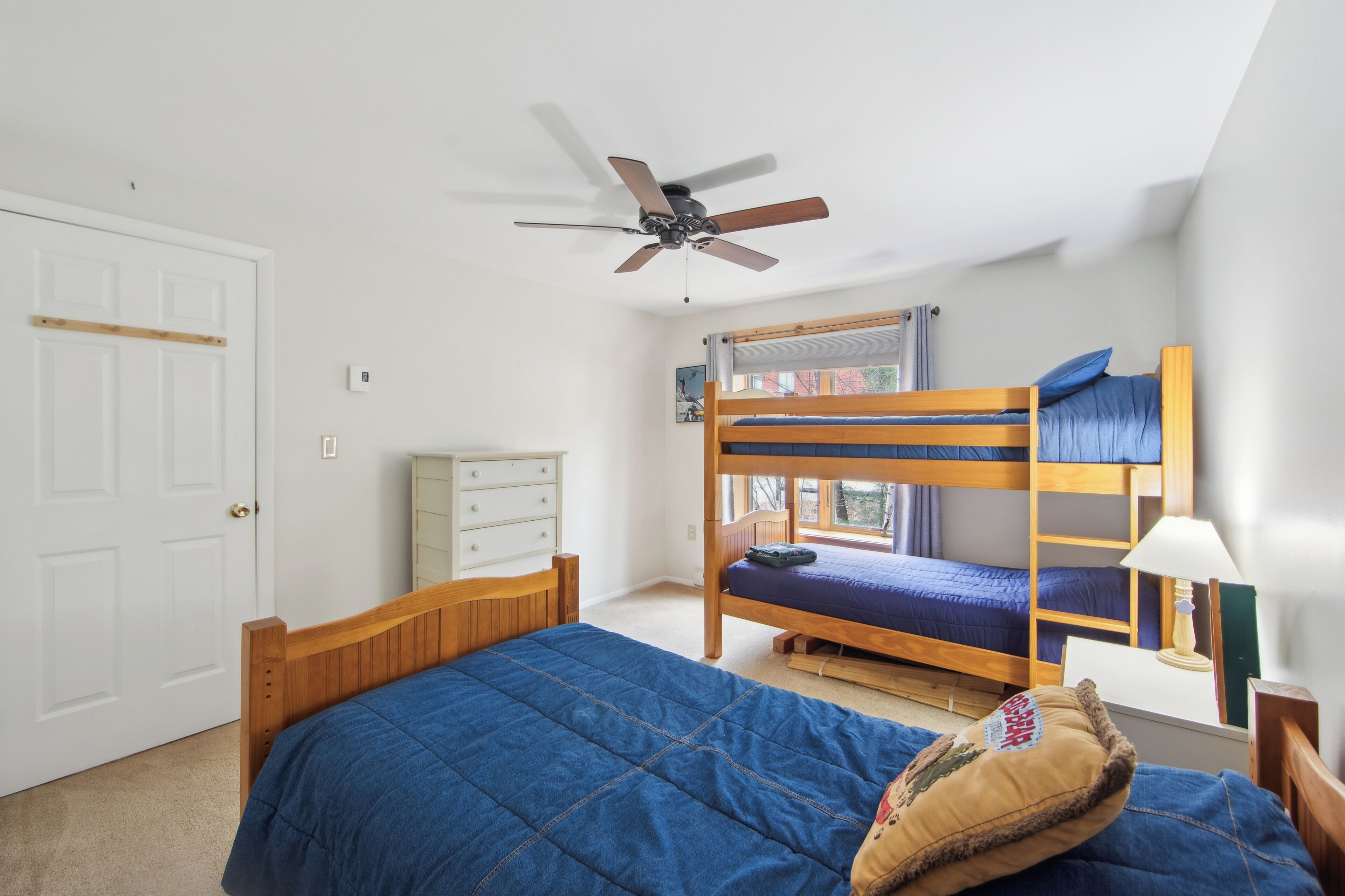 A bedroom with a bunk bed, a ceiling fan, a white dresser, and a window with a view.