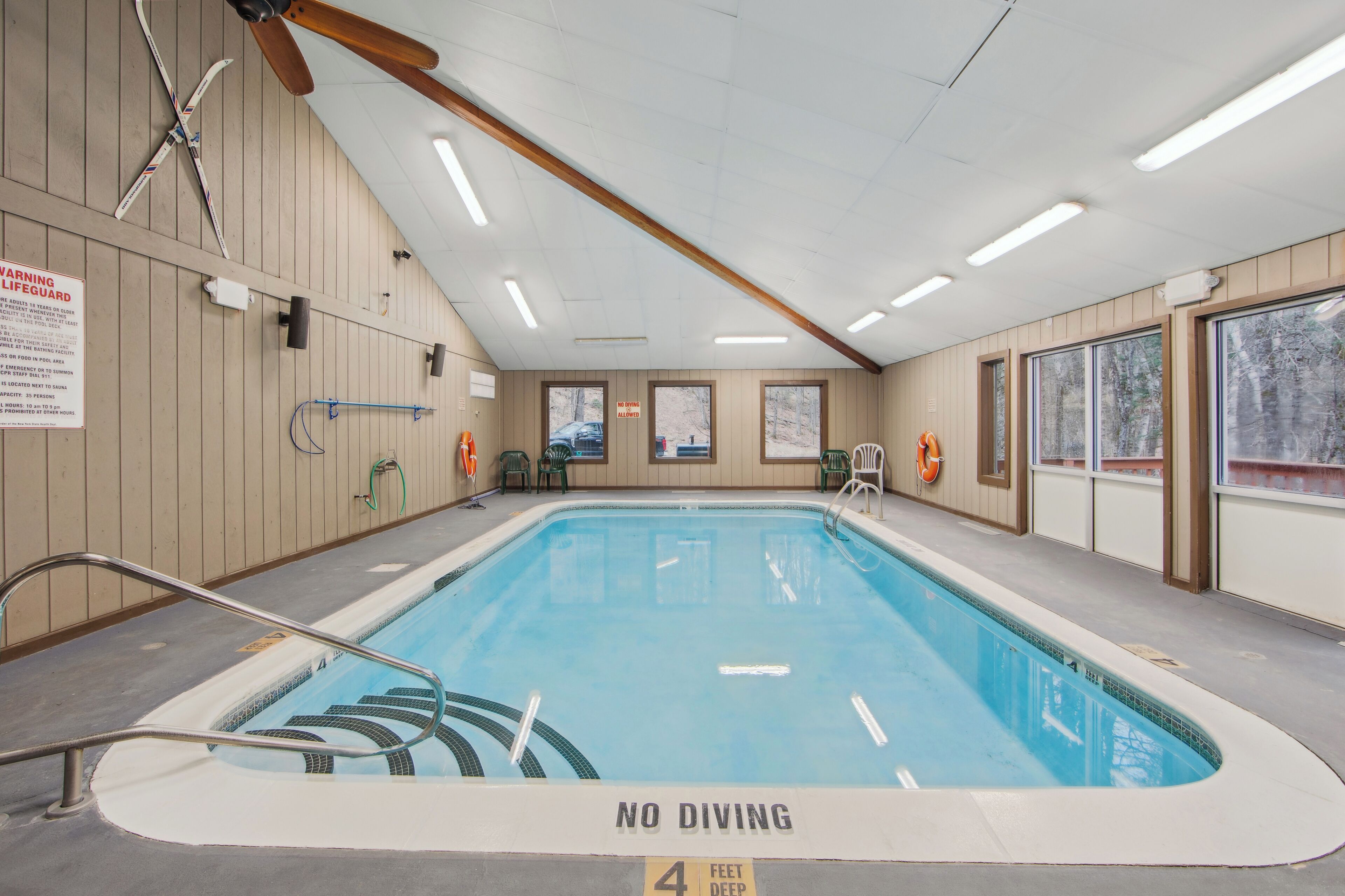Una piscina interior con un cartel de 'NO DIVING', techo de madera y un letrero de advertencia para salvavidas.