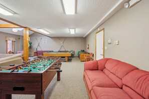 Une pièce avec une table de billard, un baby-foot et un canapé rouge.