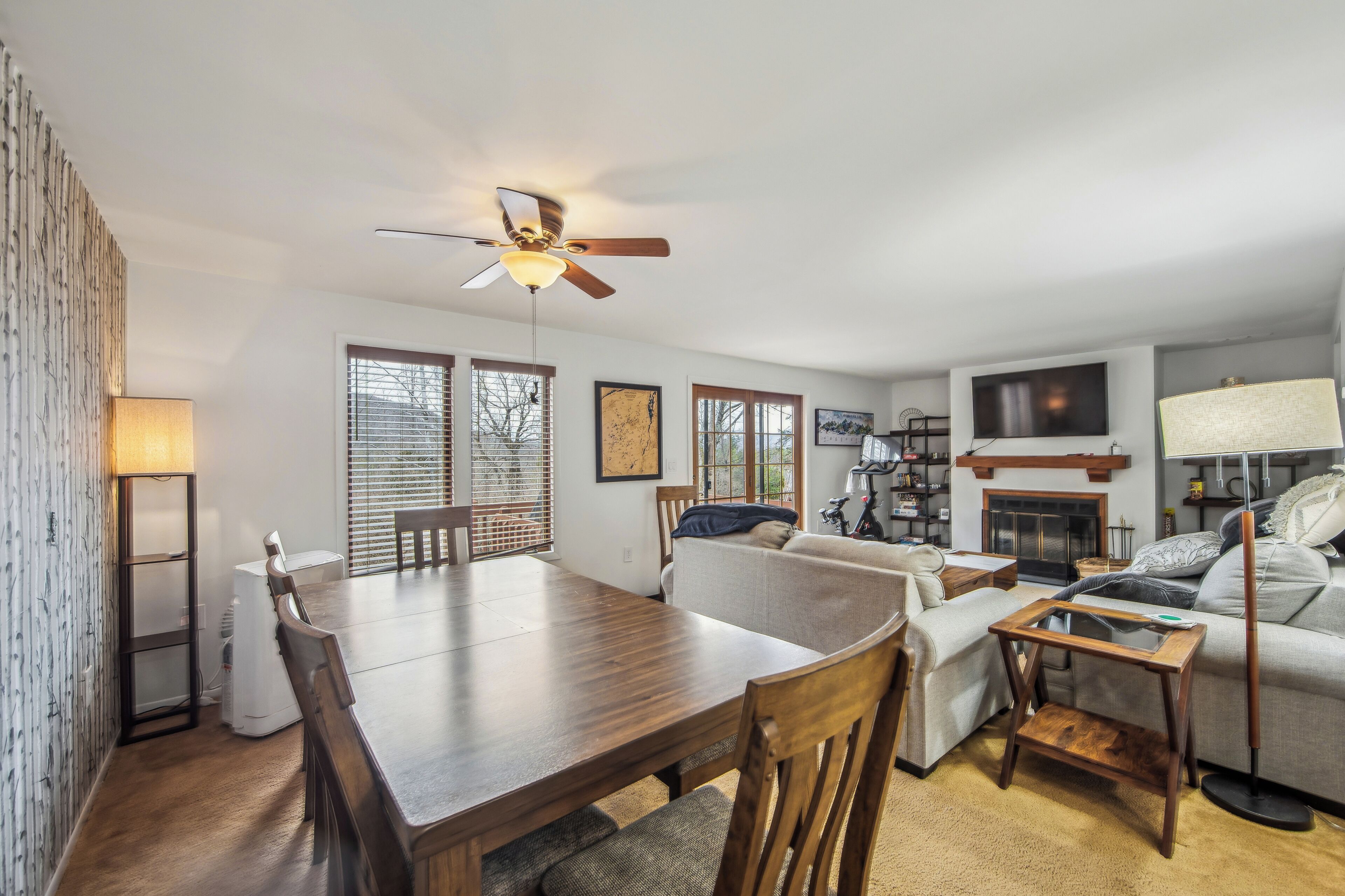 A modern living room with a dining table, sofa, TV, fireplace, and ceiling fan.