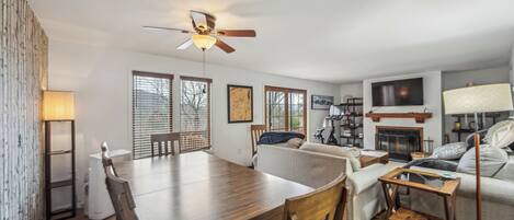 A modern living room with a dining table, sofa, TV, fireplace, and ceiling fan.