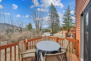 Eine Holzterrasse mit Tisch und Stühlen, mit Blick auf eine Landschaft mit Bäumen und einer entfernten Straße.