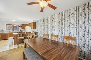 A modern kitchen with wooden cabinets, a dining table, and a ceiling fan. - 2 Townhomes + Indoor Pool + Game Room | Gore Mtn | The Summit at Gore Mtn (North Creek)