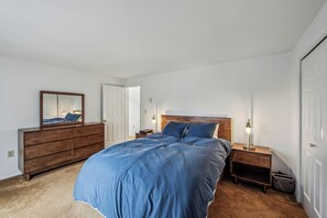 Ein Schlafzimmer mit einem großen Bett, einem Schminktisch, einem Nachttisch mit Lampe und einem Spiegel.