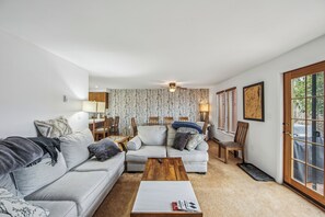 Ein Wohnzimmer mit einer Couch, einem Couchtisch und Sesseln. Eine Tür bietet Blick ins Freie.