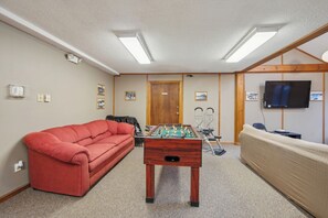 A room with a foosball table, a red sofa, a beige sofa, a television, and framed pictures on the wall. - Indoor Pool + Jetted Tub + Game Room + 2 Townhomes | The Summit at Gore Mountain (North Creek)