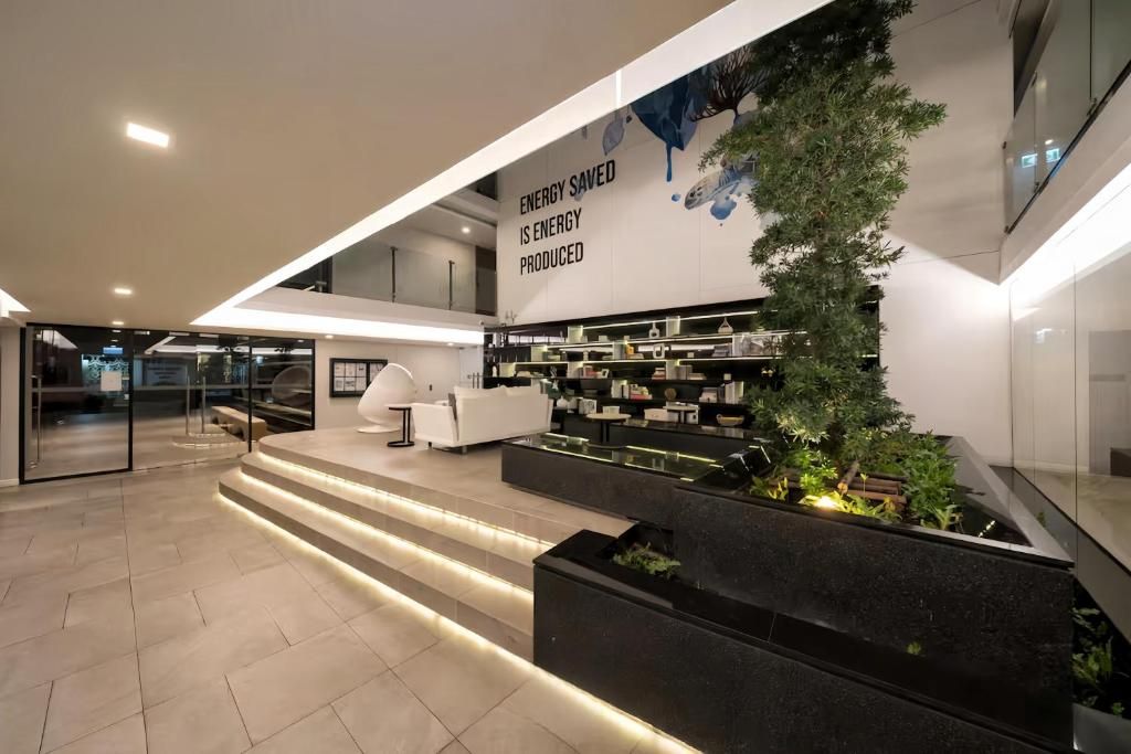 A modern lobby with a reception desk, a staircase, and a wall-mounted display about energy savings.