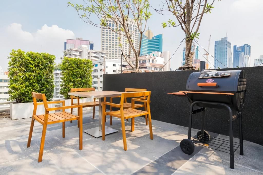 Een terras buiten met een tafel, stoelen, een barbecue en een stadsachtergrond.