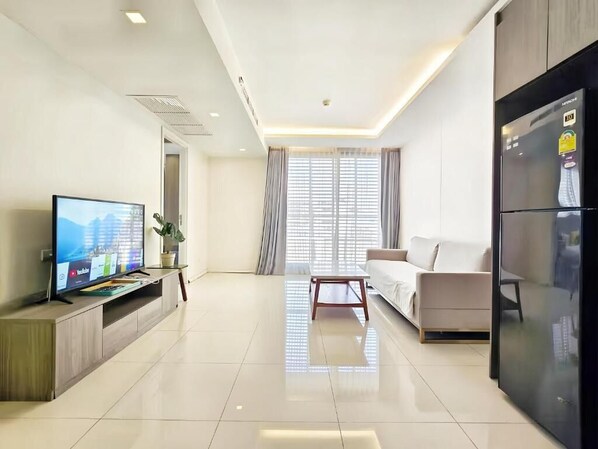 Una sala de estar moderna con un televisor de pantalla plana, un sofá, una mesa de centro y un refrigerador.