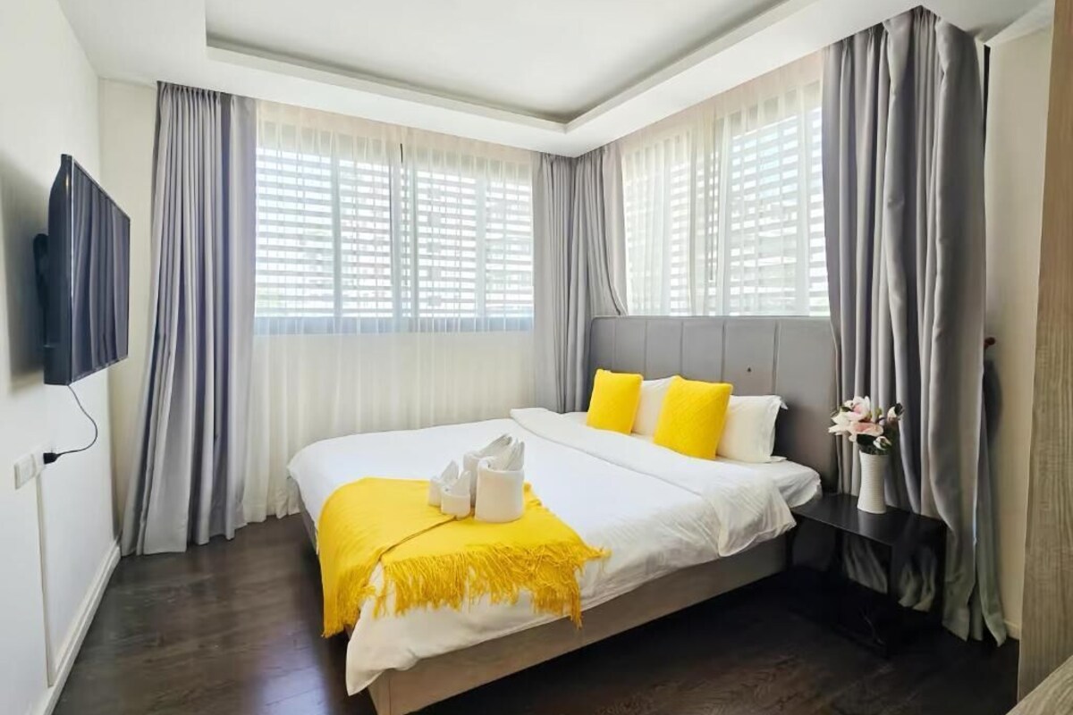 A hotel room with a large bed, a flat-screen TV, and a window with curtains.