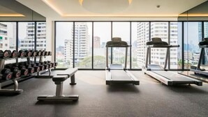 Ein Fitnessstudio mit Laufbändern, Kurzhanteln und einer Bank, große Fenster mit Blick auf die Stadt.