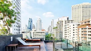 Terraza en la azotea con sillones, una mesa y baranda de vidrio con vista a la ciudad.