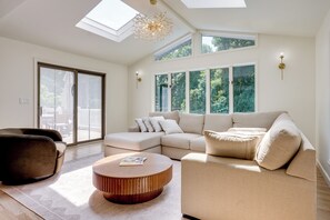 A spacious living room with a sectional sofa, a round coffee table, and a large sliding glass door leading to an outdoor area. - Furnished New City Home w/ Pool & Game Room (New City)