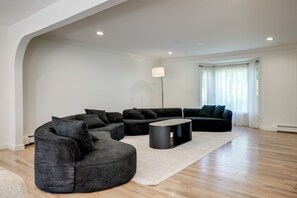 A modern living room with a sectional sofa, a round coffee table, and a floor lamp. - Furnished New City Home w/ Pool & Game Room (New City)