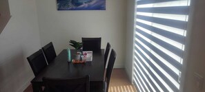 Ein Essbereich mit Tisch, Stühlen, einer Topfpflanze und einem Fenster mit Jalousien.