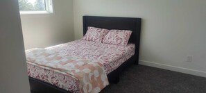 Ein Einzelbett mit dunklem Kopfteil und blumigem Bettzeug in einem Zimmer mit Fenster und Teppichboden.