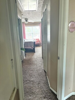 Un corridoio con tappeto che conduce a una camera da letto, con un letto, una finestra con tende e una porta con il cartello 'VIP Lounge'.