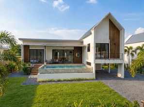 Ein modernes, zweistöckiges Haus mit Swimmingpool, überdachter Terrasse und gepflegtem Rasen.