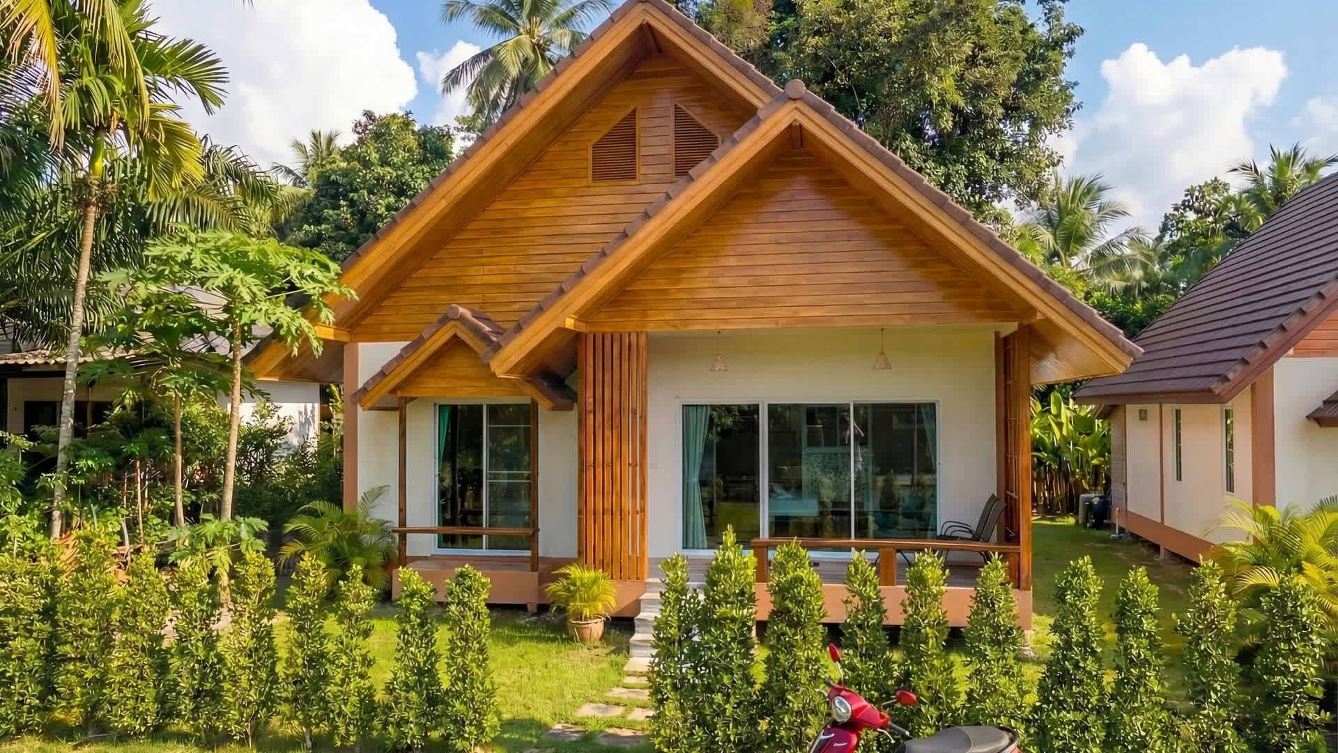 Un bungalow doté d’un toit en pente, de grandes fenêtres et d’un jardin planté de plantes tropicales.