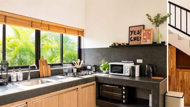 Een moderne keuken met een ingebouwde oven, magnetron en een groot raam met uitzicht op groen.