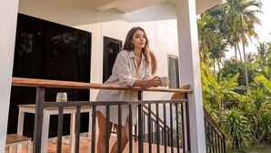 Une personne se tient sur un balcon, avec une balustrade, une table et des chaises en contrebas.