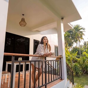A person standing on a balcony with a railing, a table, and chairs below.