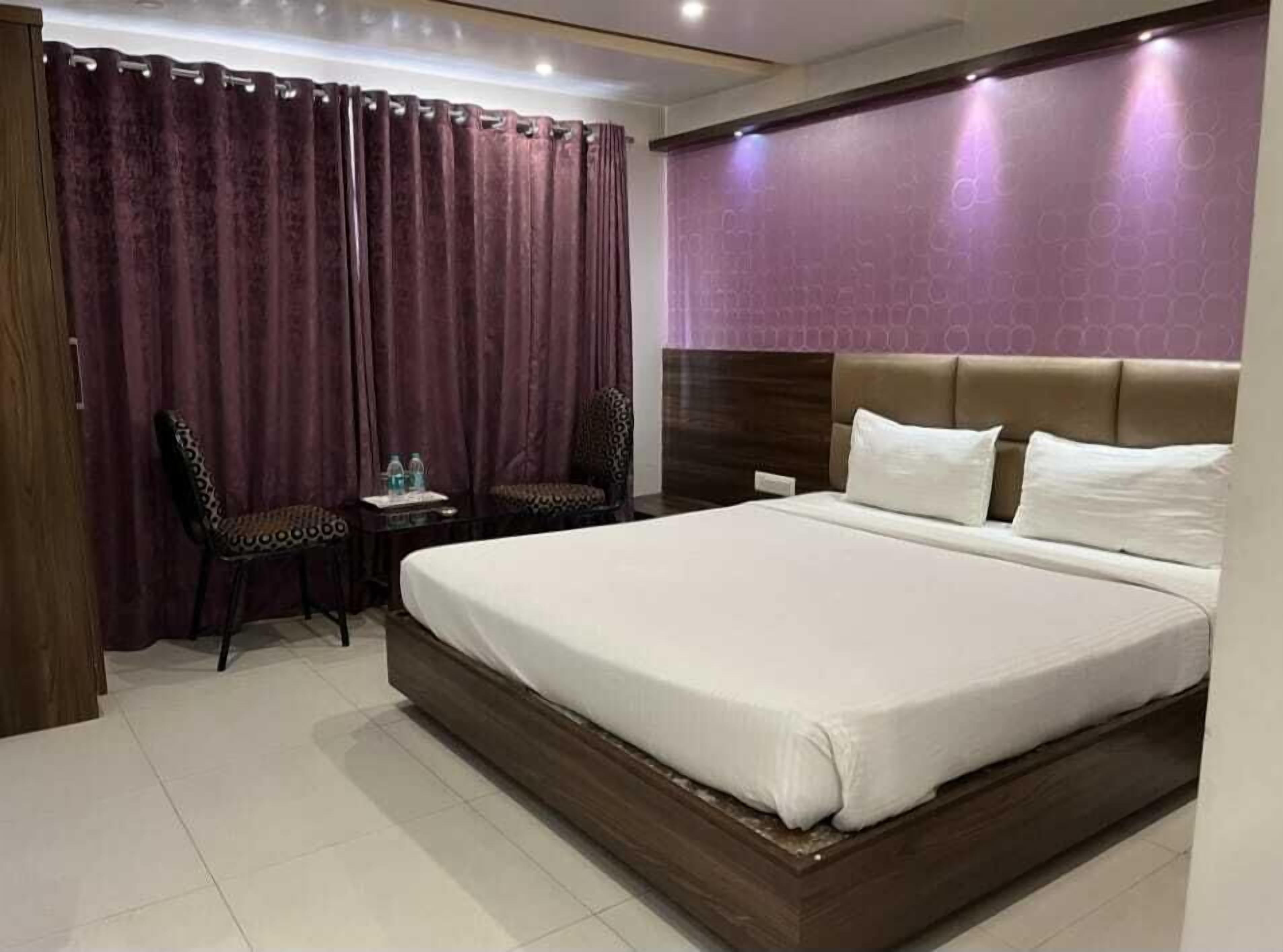 Una habitación de hotel con una cama grande, una mesita de noche, una silla y una cortina.