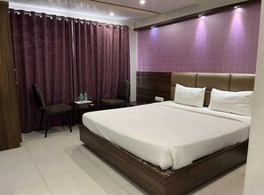 Una habitación de hotel con una cama grande, una mesita de noche, una silla y una cortina.