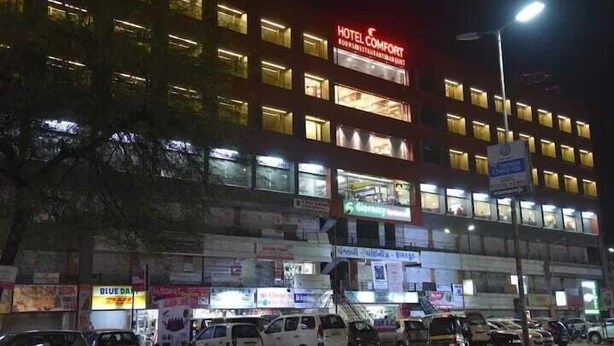 Un hôtel à plusieurs étages, doté d’une enseigne lumineuse, d’un parking et de divers commerces au rez-de-chaussée.