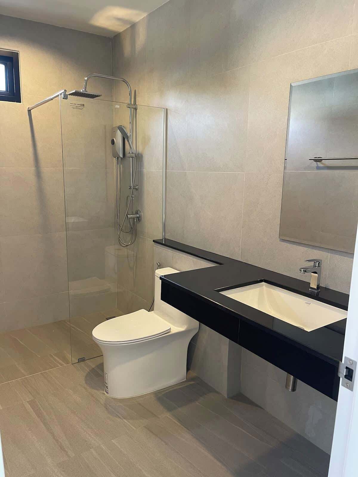 Ein modernes Badezimmer mit einer in Glas abgeschlossenen Dusche, einer weißen Toilette und einer schwarzen Ablage mit Waschbecken.