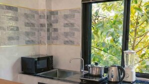 A modern kitchen with a microwave, stove, and blender on the counter, a window with a view of greenery, and a tiled backsplash. - Garden Villa Green View Central Location (Srithanu Beach)