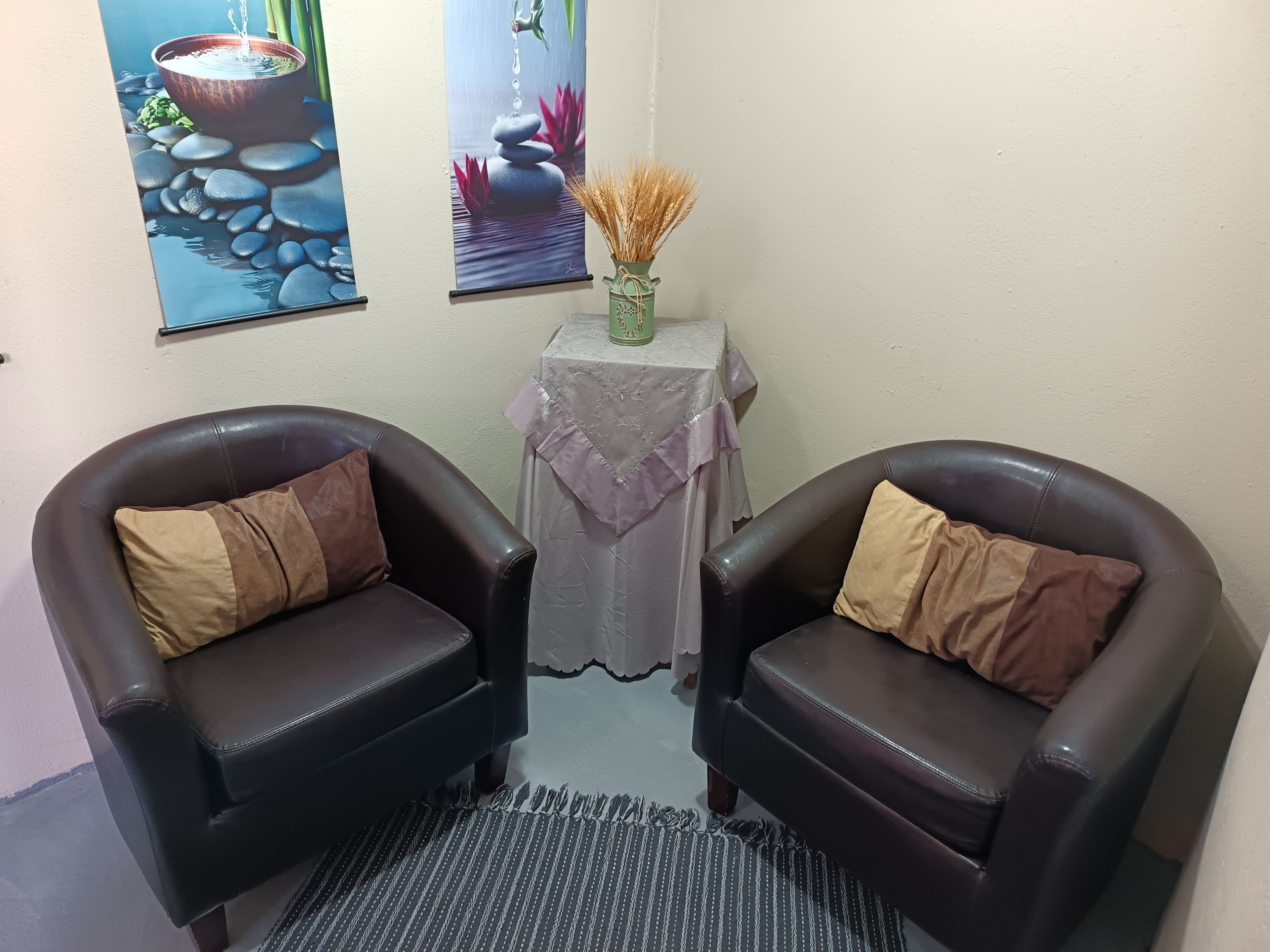 Une pièce comprenant deux fauteuils en cuir, une petite table sur laquelle est posé un vase contenant des plantes séchées, et deux œuvres d’art encadrées accrochées au mur.