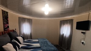 Un dormitorio con cama, cortinas, televisor y luz de techo.