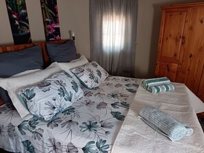 Una cama bien hecha con ropa de cama floral, un armario de madera y una ventana con cortinas.