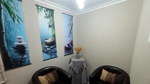 Una habitación con dos sillones de cuero negro, una mesita con un jarrón de flores y tres cuadros verticales que representan paisajes naturales.