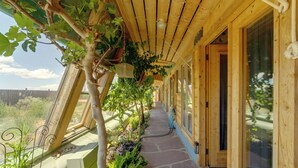 A covered wooden walkway with a stone floor, surrounded by various plants and a view of the landscape. - Serene, Family-Sized Off Grid Earthship w/ Big Mtn (Tres Piedras)