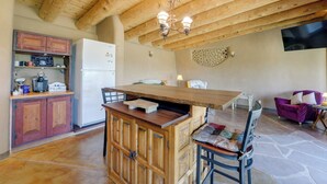 A kitchen with wooden beams, a refrigerator, a coffee station, and a dining area with a table and chairs. - Serene, Family-Sized Off Grid Earthship w/ Big Mtn (Tres Piedras)