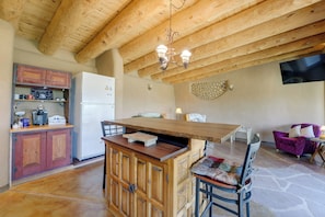 A kitchen with wooden beams, a refrigerator, a coffee station, and a dining area with a table and chairs. - Serene, Family-Sized Off Grid Earthship w/ Big Mtn (Tres Piedras)
