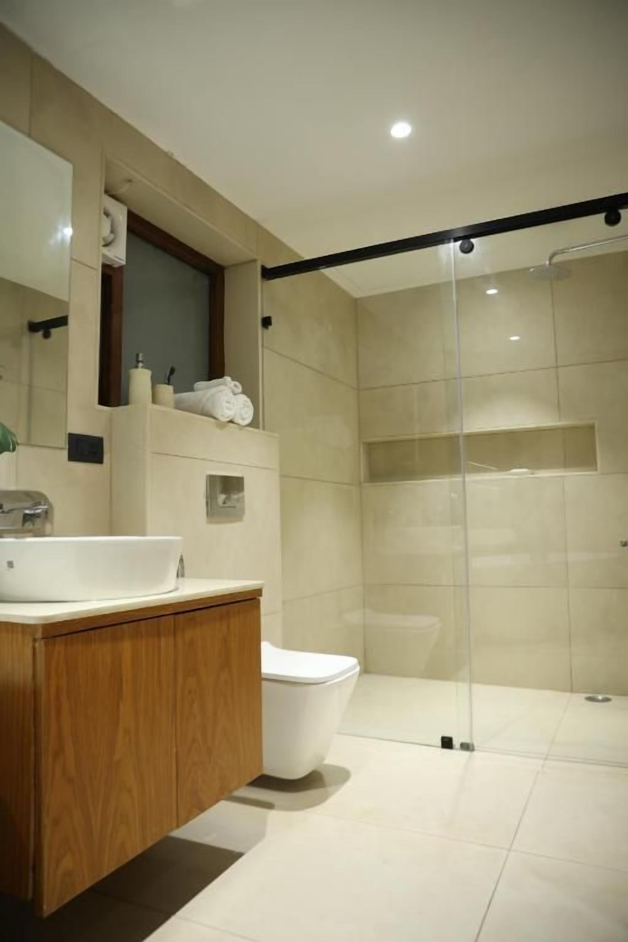 A modern bathroom with a glass shower enclosure, a wooden vanity, and a white toilet.
