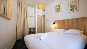 Une chambre d’hôtel avec un grand lit, une tête de lit en bois, une lampe fixée au mur et deux tableaux encadrés.