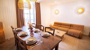 A dining area with a wooden table set for four, a sofa, and a wall-mounted light fixture. - La Maison Momiji - Elegance and the Art of Living (Tours)