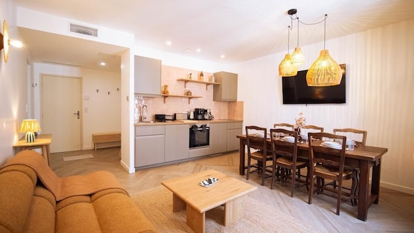 A modern living room with a sofa, a small wooden table, and a dining area with a wooden table and chairs. - La Maison Momiji - Elegance and the Art of Living (Tours)